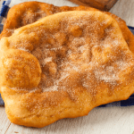 Golden, freshly fried dough sprinkled with powdered sugar, perfect for recreating a classic fairground dessert at home.