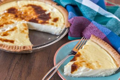 Creamy Old Fashioned Egg Custard Pie Recipe: A Classic Comfort Dessert 92 Old Fashioned Custard Pie in a glass pie dish with a golden-brown crust and rich custard filling. A slice is plated on a blue and orange plate, ready to be enjoyed with whipped cream or as is.