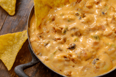 How to Make Rotel Dip: Easy Rotel Dip Recipe for a Tasty Chili Cheese Dip 110 A close-up view of a thick, orange cheese dip filled with meat and chiles in a cast-iron skillet, surrounded by crunchy tortilla chips.